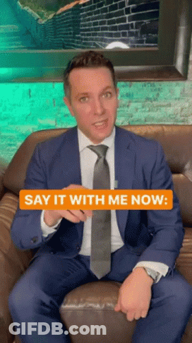 A Man In A Suit And Tie Is Sitting On A Couch With The Words Say It With Me Now GIF