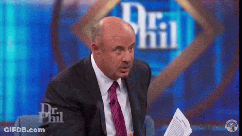 A Man In A Suit And Tie Is Sitting On A Stage In Front Of A Dr Phil Logo . GIF