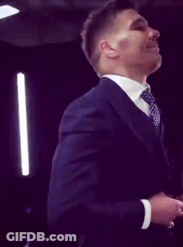 A Man In A Suit And Tie Is Smiling And Adjusting His Jacket GIF