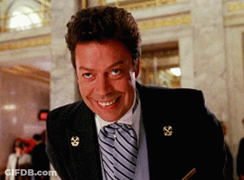A Man In A Suit And Tie Is Smiling And Looking At The Camera GIF