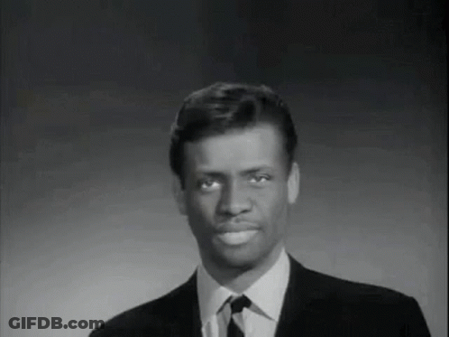 A Man In A Suit And Tie Is Smiling And Looking At The Camera . GIF