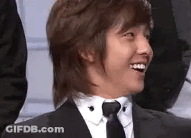 A Man In A Suit And Tie Is Smiling And Looking At The Camera . GIF