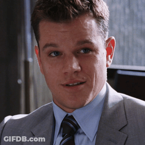 A Man In A Suit And Tie Is Smiling And Looking At The Camera GIF