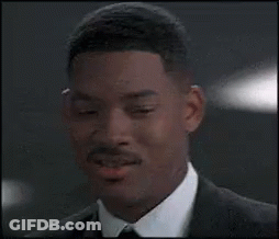A Man In A Suit And Tie Is Smiling And Looking At The Camera . GIF
