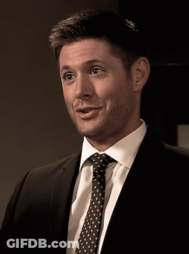 A Man In A Suit And Tie Is Smiling And Looking At The Camera GIF