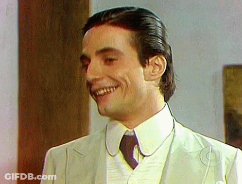A Man In A Suit And Tie Is Smiling And Looking At The Camera GIF