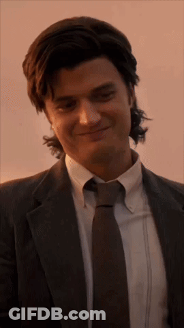 A Man In A Suit And Tie Is Smiling And Looking At The Camera . GIF