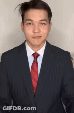 A Man In A Suit And Tie Is Smiling And Looking At The Camera . GIF
