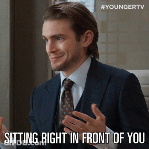 A Man In A Suit And Tie Is Smiling And Sitting Right In Front Of You GIF