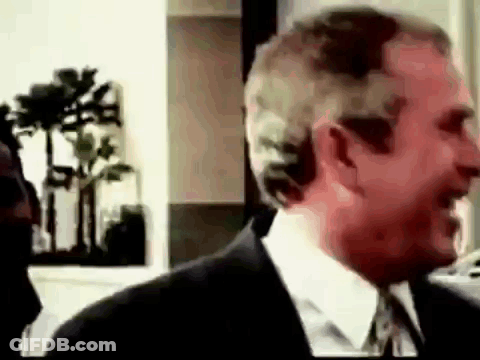 A Man In A Suit And Tie Is Smiling And Talking To Another Man . GIF