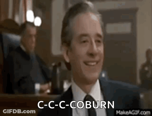 A Man In A Suit And Tie Is Smiling In A Courtroom While Another Man Sits Behind Him . GIF