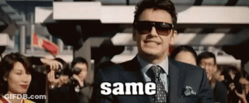 A Man In A Suit And Tie Is Smiling In Front Of A Crowd While Wearing Sunglasses . GIF