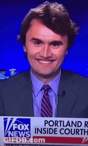 A Man In A Suit And Tie Is Smiling In Front Of A Fox News Banner GIF