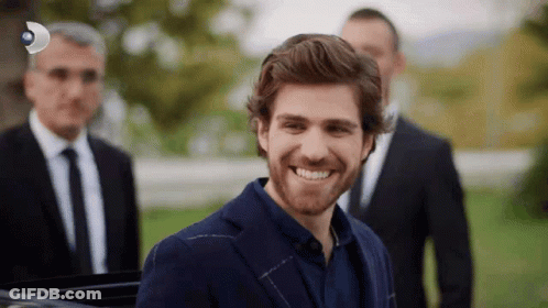 A Man In A Suit And Tie Is Smiling In Front Of A Group Of Men In Suits GIF