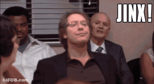 A Man In A Suit And Tie Is Smiling In Front Of A Group Of People And The Word Jinx Is Above Him GIF