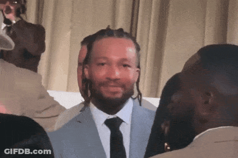 A Man In A Suit And Tie Is Smiling In Front Of A Group Of People GIF