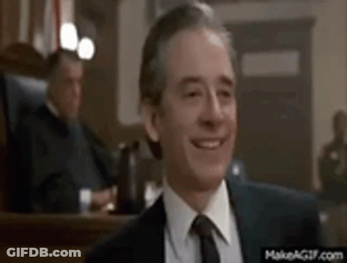 A Man In A Suit And Tie Is Smiling In Front Of A Judge In A Courtroom . GIF