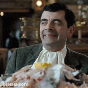 A Man In A Suit And Tie Is Smiling In Front Of A Pile Of Food With GIF-Finder.com In The Corner GIF
