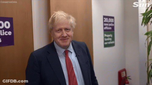A Man In A Suit And Tie Is Smiling In Front Of A Sign That Says Conservatives On It GIF