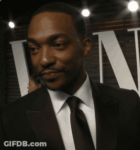 A Man In A Suit And Tie Is Smiling In Front Of A Sign That Says Tn GIF