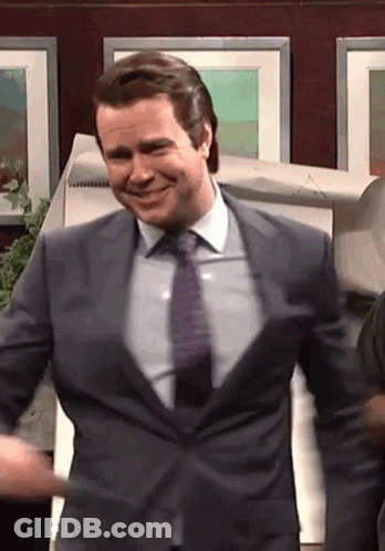 A Man In A Suit And Tie Is Smiling In Front Of A Wall Of Pictures GIF