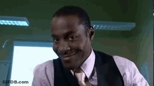 A Man In A Suit And Tie Is Smiling In Front Of A Window . GIF