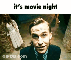A Man In A Suit And Tie Is Smiling In Front Of A Woman In A White Dress And The Words It 'S Movie Night Below Him GIF