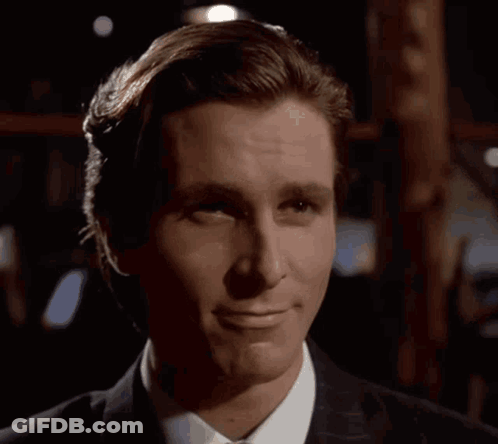 A Man In A Suit And Tie Is Smiling In The Dark GIF