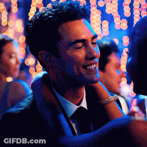 A Man In A Suit And Tie Is Smiling While Holding A Woman 'S Arm GIF