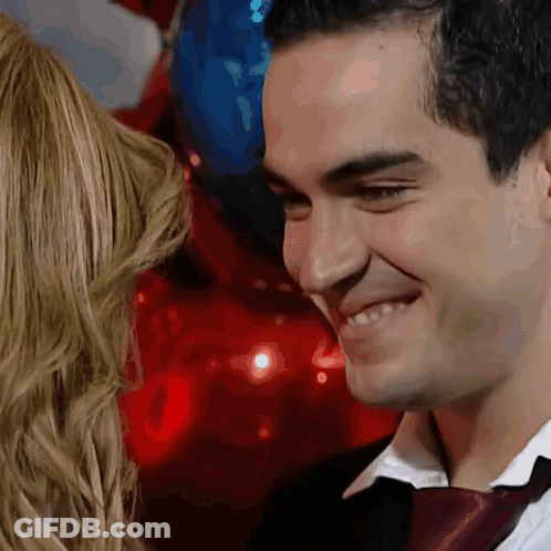 A Man In A Suit And Tie Is Smiling While Looking At A Woman GIF