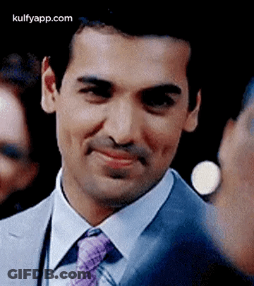 A Man In A Suit And Tie Is Smiling While Looking At The Camera . GIF