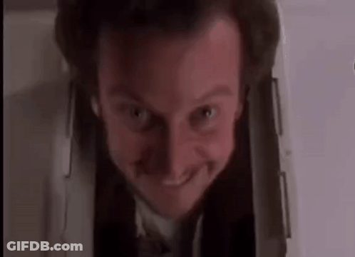 A Man In A Suit And Tie Is Smiling While Looking Out Of A Hole In The Wall . GIF