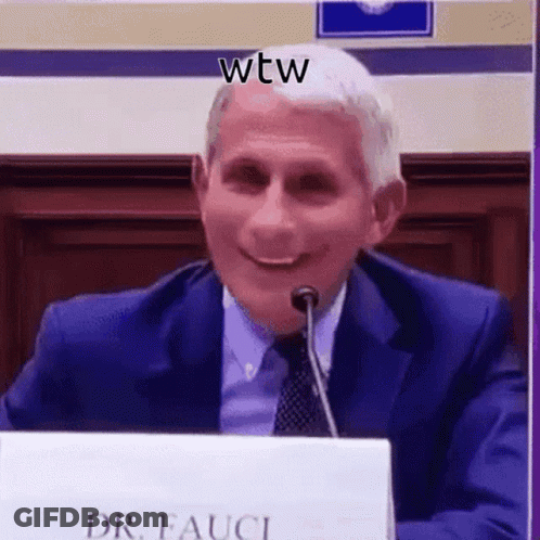 A Man In A Suit And Tie Is Smiling While Sitting At A Table With A Microphone . GIF
