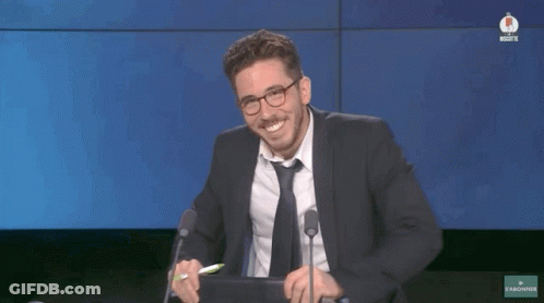 A Man In A Suit And Tie Is Smiling While Sitting In Front Of A Microphone GIF
