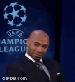 A Man In A Suit And Tie Is Smiling While Sitting In Front Of A Sign That Says Uefa Champions League . GIF