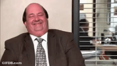 A Man In A Suit And Tie Is Smiling While Sitting In Front Of A Window In An Office . GIF