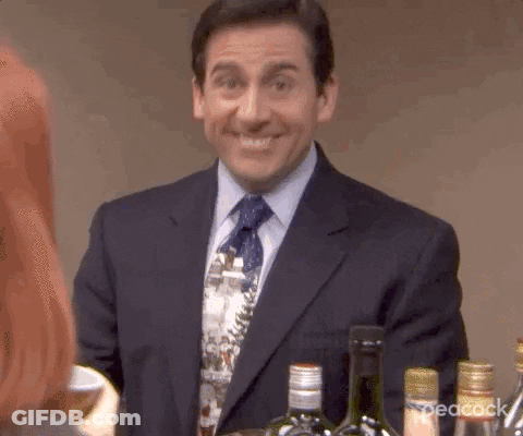 A Man In A Suit And Tie Is Smiling While Standing Next To A Bottle Of Wine . GIF