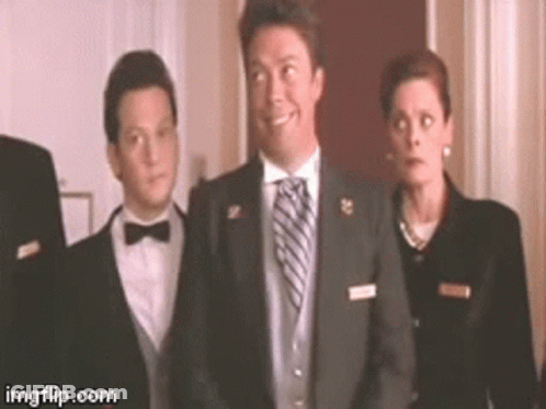 A Man In A Suit And Tie Is Smiling While Standing Next To A Woman In A Suit . GIF