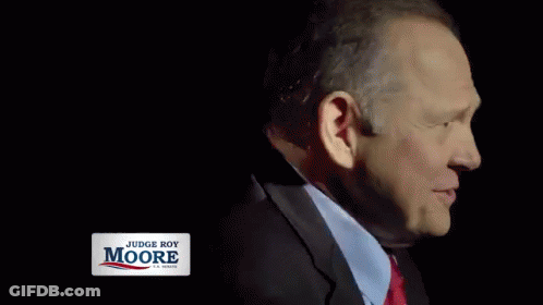 A Man In A Suit And Tie Is Smiling With A Judge Roy Moore Sign Behind Him GIF