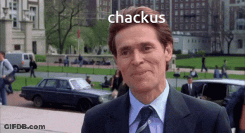 A Man In A Suit And Tie Is Smiling With The Word Chackus Behind Him GIF