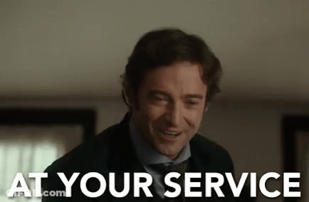 A Man In A Suit And Tie Is Smiling With The Words `` At Your Service '' Written Next To Him . GIF