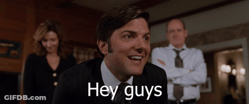 A Man In A Suit And Tie Is Smiling With The Words Hey Guys Below Him GIF