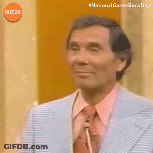 A Man In A Suit And Tie Is Smiling With The Words National Game Show Day Below Him GIF