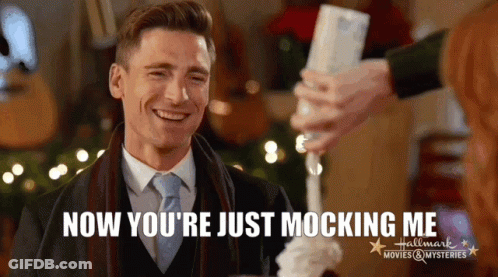A Man In A Suit And Tie Is Smiling With The Words Now You 'Re Just Mocking Me Behind Him GIF