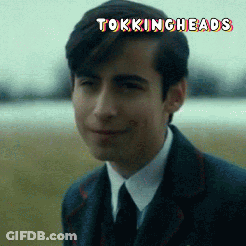 A Man In A Suit And Tie Is Smiling With The Words Tokingheads Written Above Him GIF
