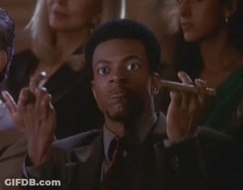 A Man In A Suit And Tie Is Smoking A Cigar In Front Of A Crowd . GIF