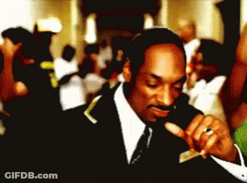 A Man In A Suit And Tie Is Smoking A Cigarette In Front Of A Crowd GIF