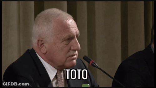 A Man In A Suit And Tie Is Speaking Into A Microphone And The Word Toto Is On The Screen Behind Him GIF