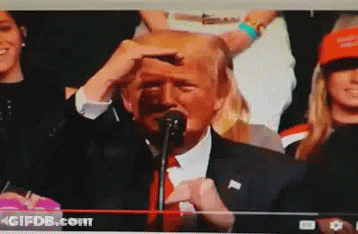 A Man In A Suit And Tie Is Speaking Into A Microphone In Front Of A Crowd GIF