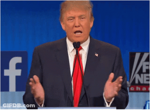 A Man In A Suit And Tie Is Speaking Into A Microphone In Front Of A Facebook Sign GIF
